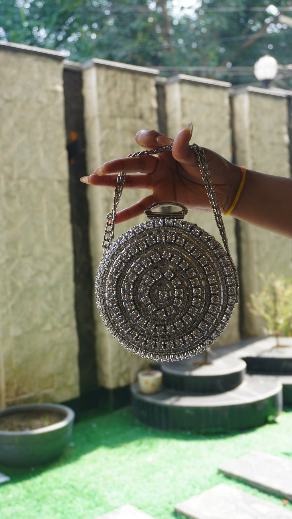 Silver circular crystal bridal clutch showing decorative top clasp and chain carry handle