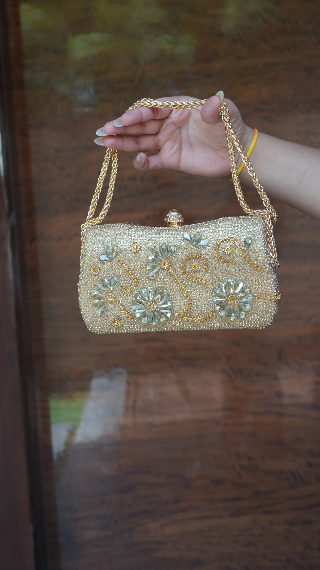 Golden floral embroidered clutch showing decorative top clasp and chain handle