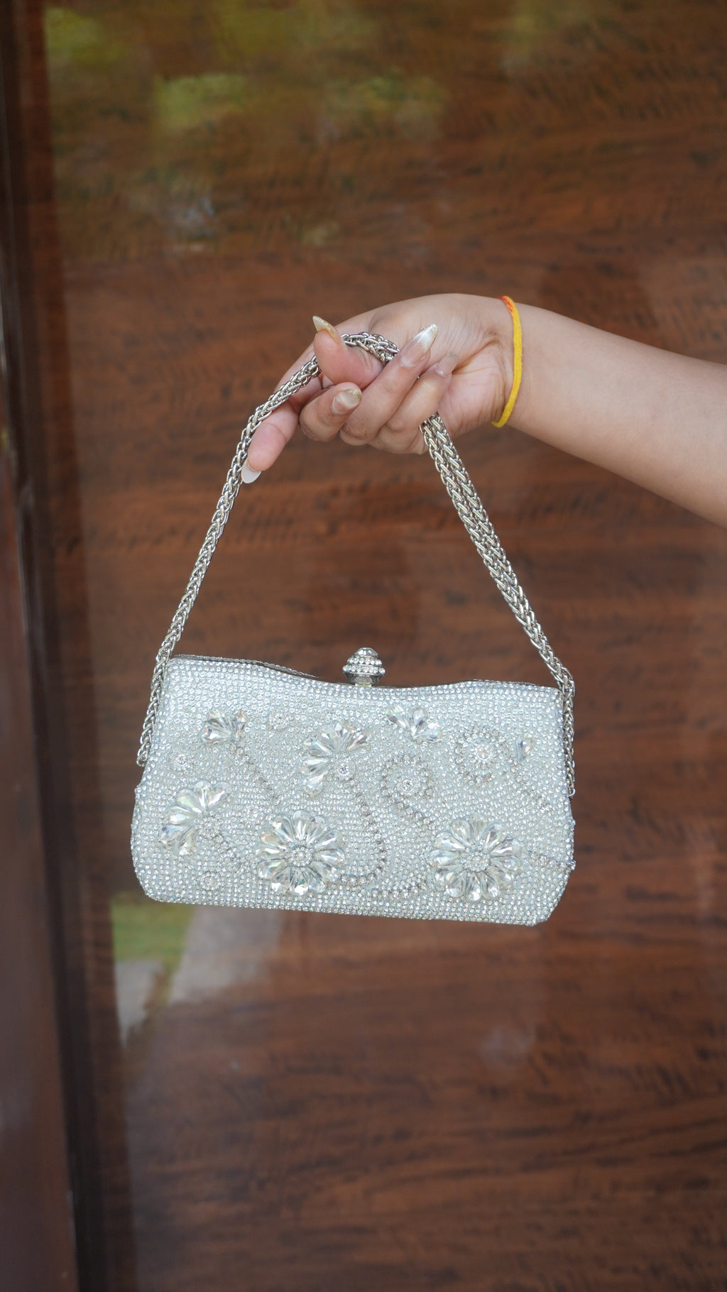 Silver floral embroidered clutch showing decorative top clasp and chain handle