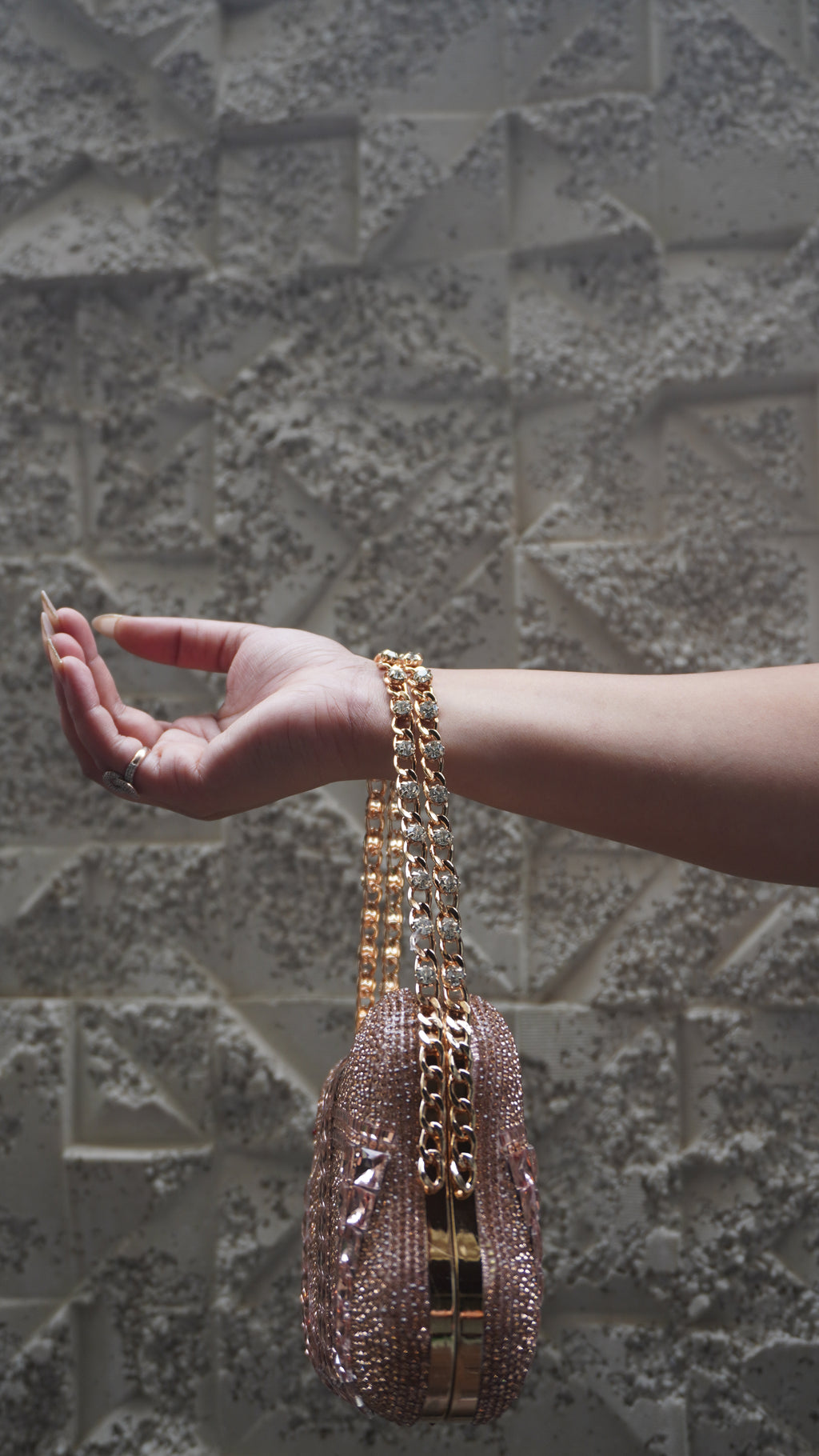 Side view of rose pink embellished clutch with gold-toned frame and chain handle