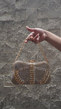 Golden embellished party clutch with chain handle and bow-shaped top clasp