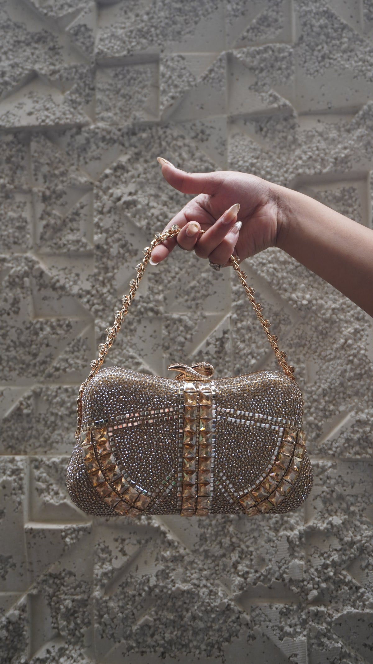 Golden embellished party clutch with chain handle and bow-shaped top clasp