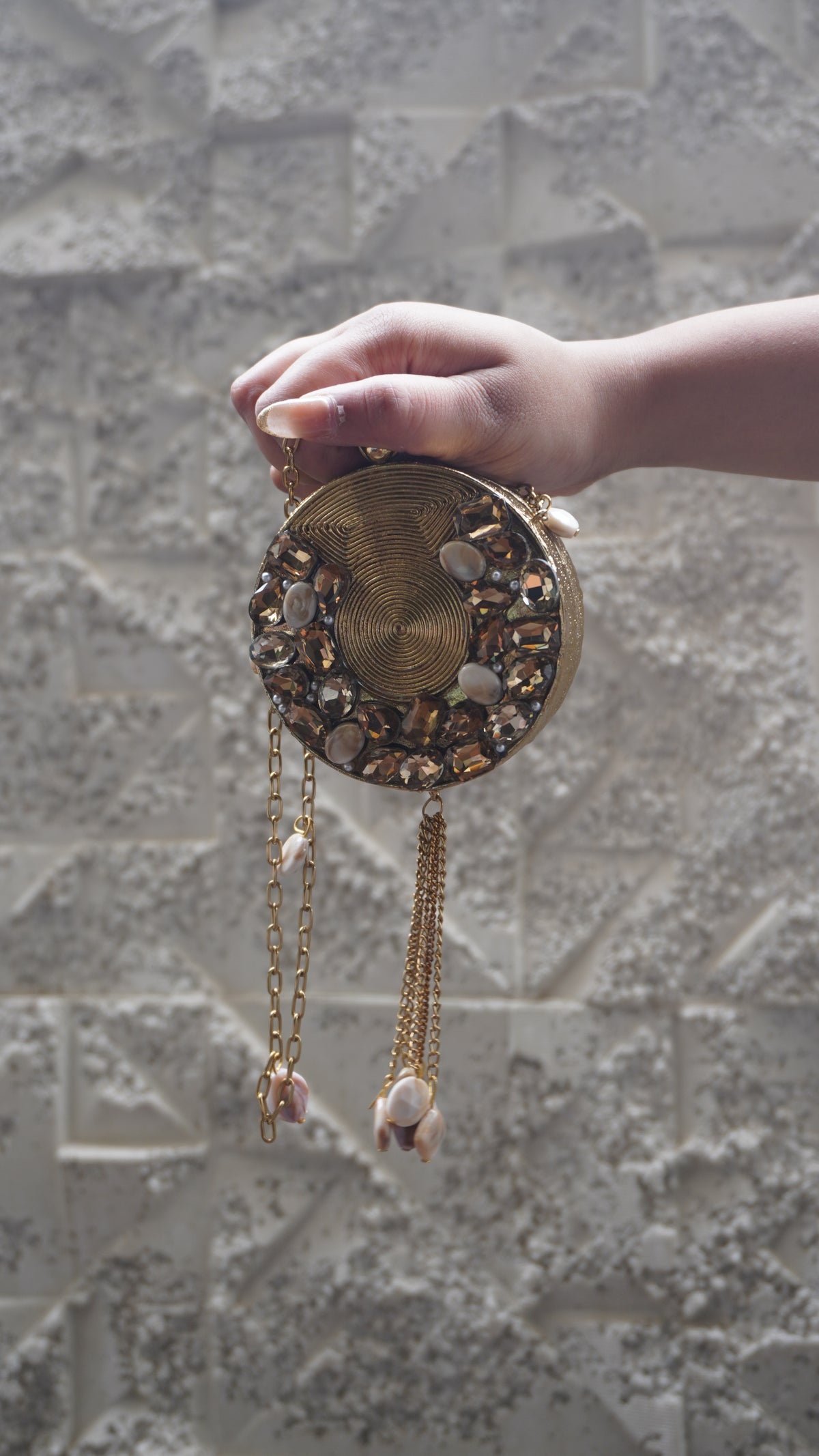 Golden brass round sling bag showing spiral detailing, faceted embellishments and chain tassel