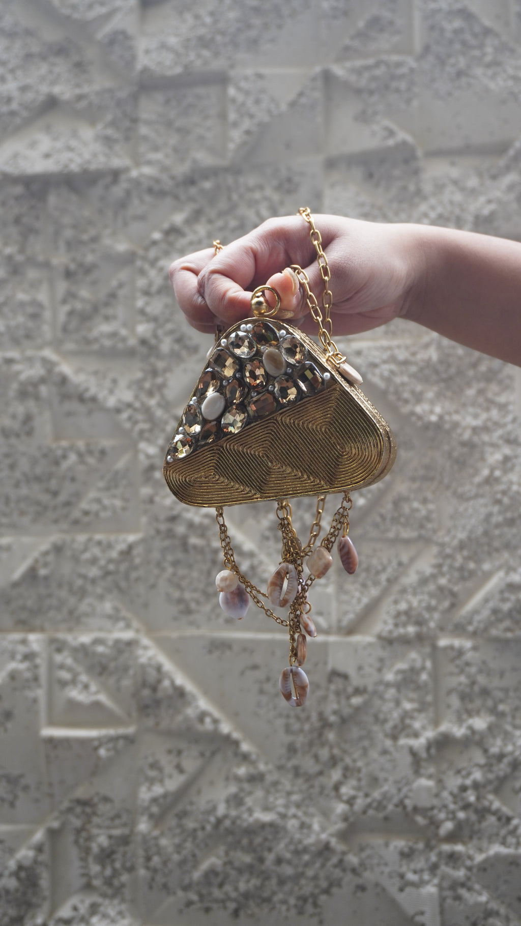 Golden brass triangle sling bag showing textured detailing and pale oval accents