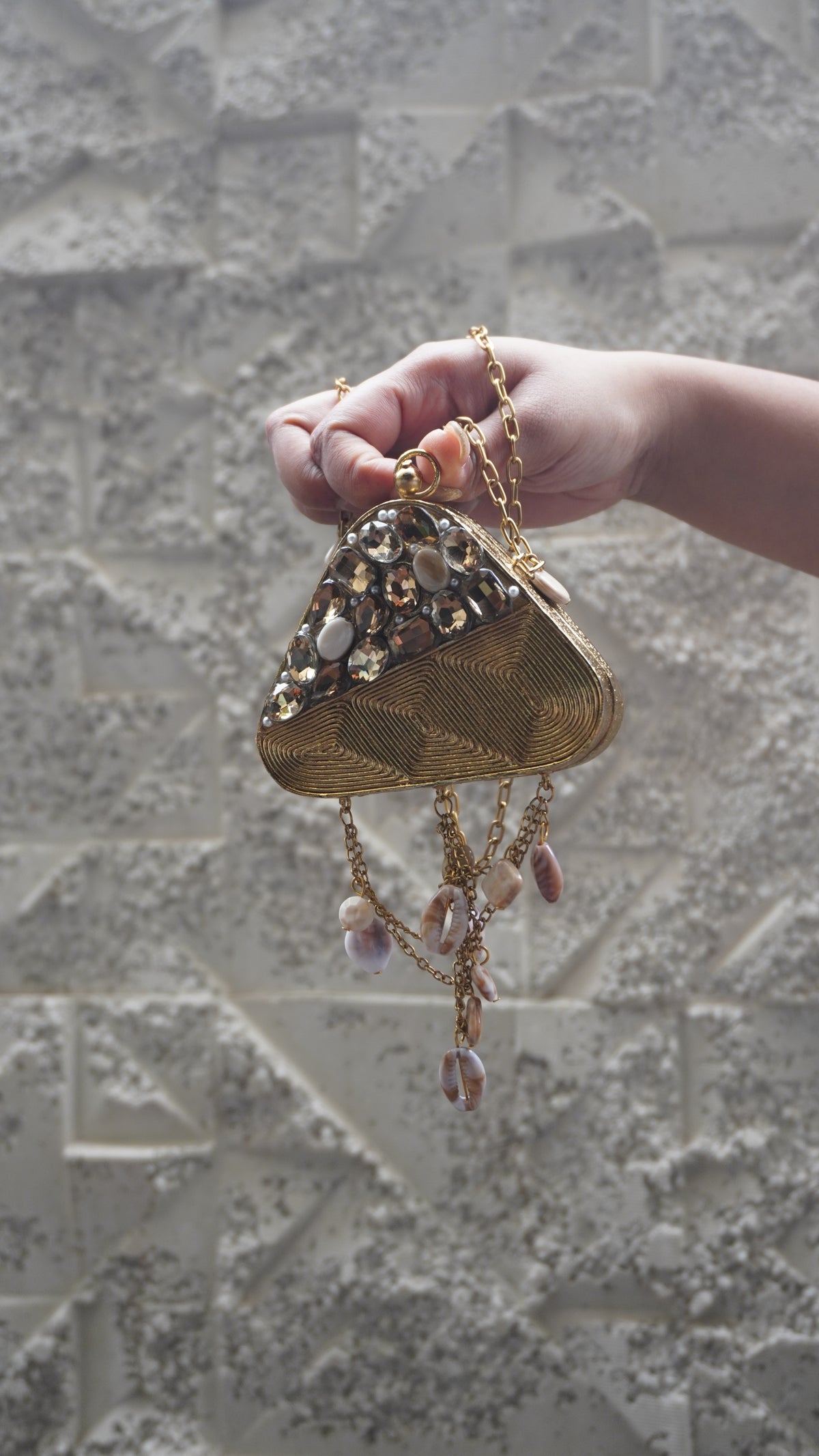 Golden brass triangle sling bag showing textured detailing and pale oval accents